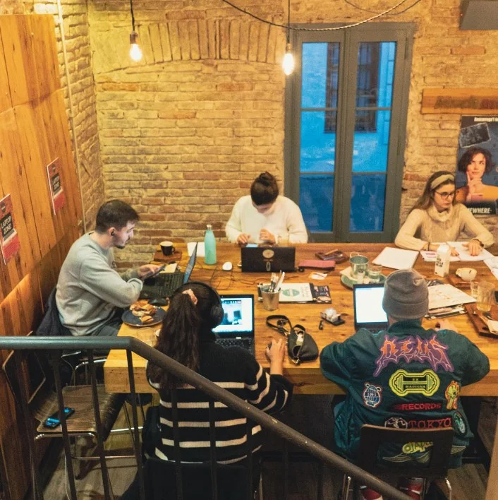 People working on laptops around a long wooden table in the café