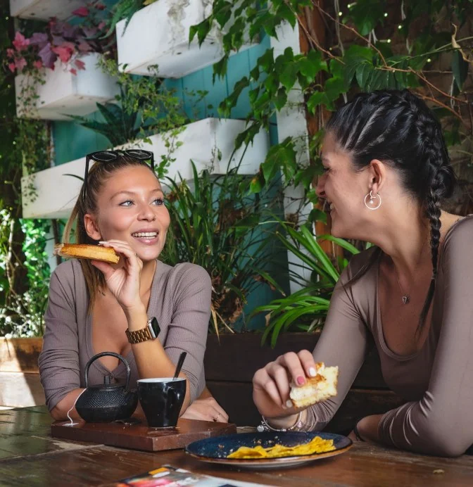 Two friends laughing over tea and toast among the plants