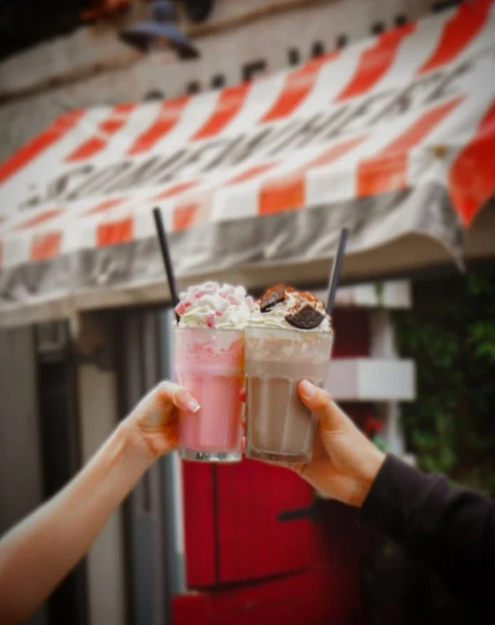 Two milkshakes raised in a toast under the striped awning